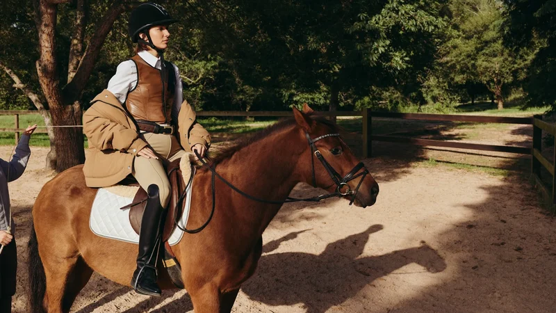Bambino con il casco in sella a un pony nel paddock, accompagnato da un adulto